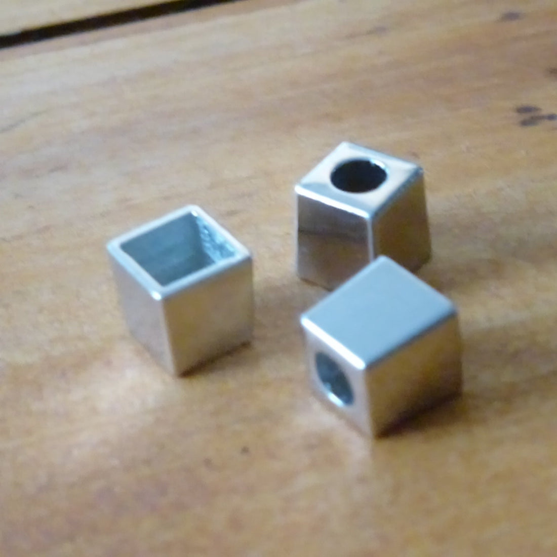 Three metallic cube-shaped cord ends on a wooden surface