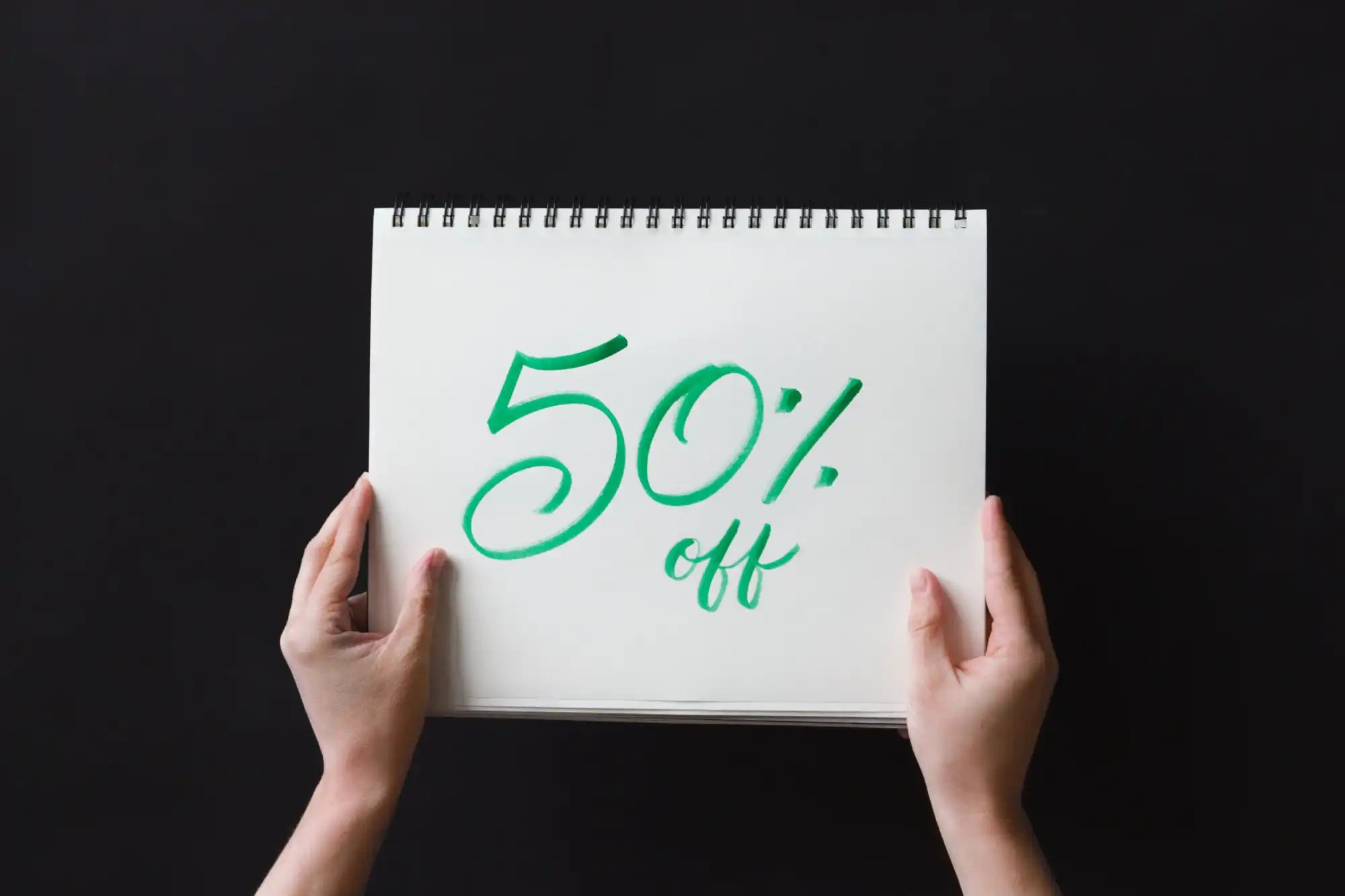 Hands holding a notepad displaying ’50% off’ written in green ink.