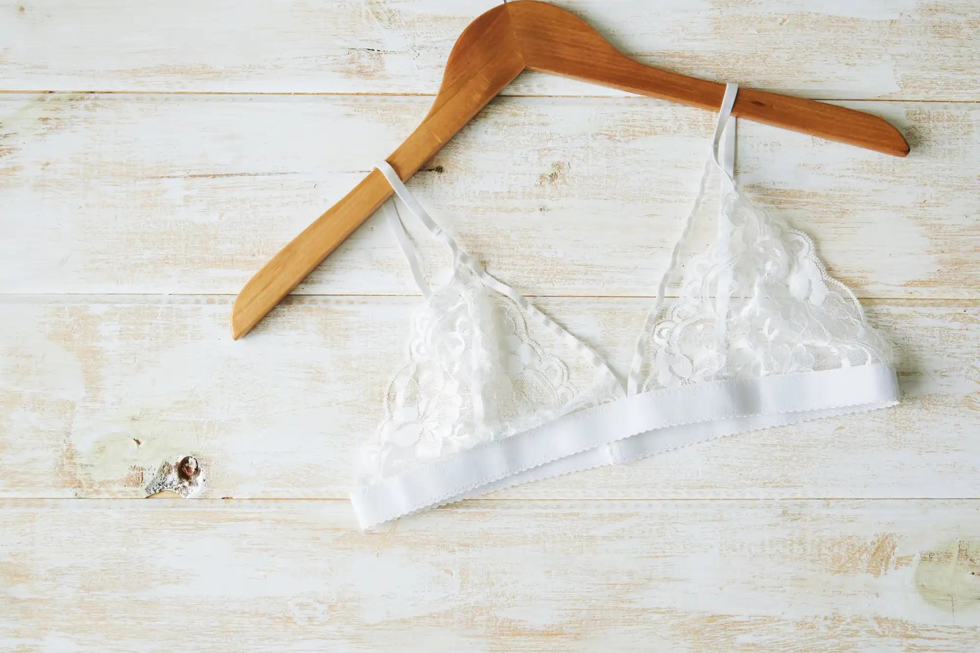 White lace bralette hanging on a wooden hanger.